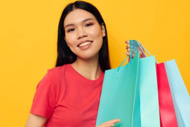 Asyalı güzel bir kadın portresi. Çok renkli alışveriş çantaları var. Sarı arka plan değişmemiş.