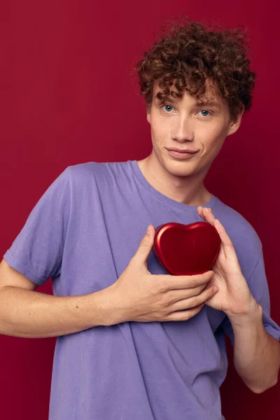 Roztomilý kudrnatý chlap v fialové tričko srdce ve tvaru krabice dárek — Stock fotografie