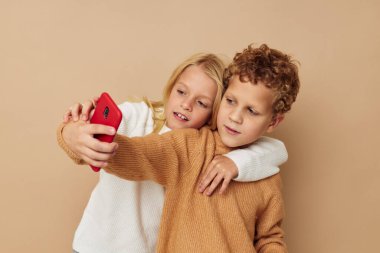 Telefonla izole edilmiş arka planda eğlenmek için poz veren kazaklı iki çocuğun fotoğrafı.