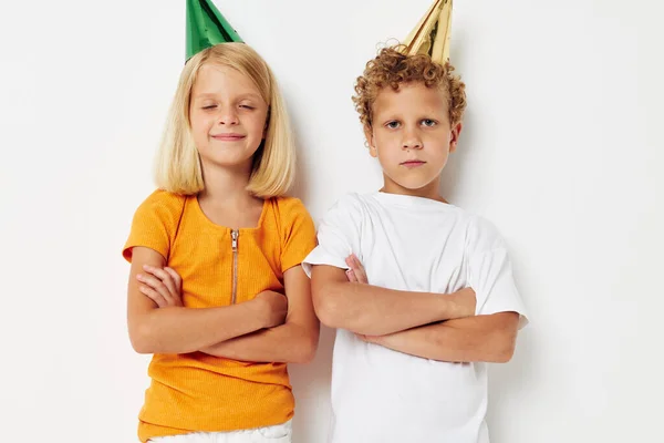 Két vidám gyermek pózol érzelmek ünnep színes sapkák fény háttér — Stock Fotó