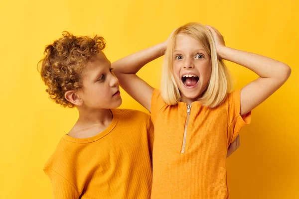 Два радостных ребенка в желтых футболках стоят бок о бок детские эмоции желтый фон — стоковое фото