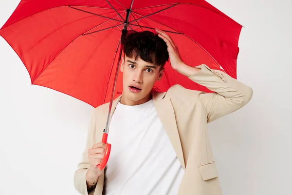 Porträt eines jungen Mannes, der einen Regenschirm in den Händen hält und dabei vor hellem Hintergrund posiert — Stockfoto