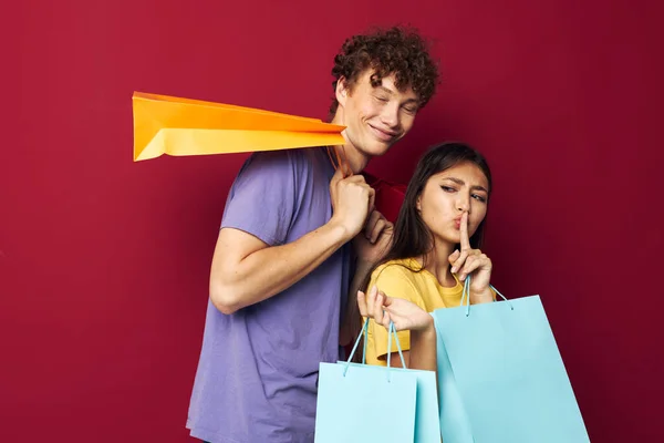 Schattig jong stel in kleurrijke T-shirts met tassen Shopping rode achtergrond ongewijzigd — Stockfoto