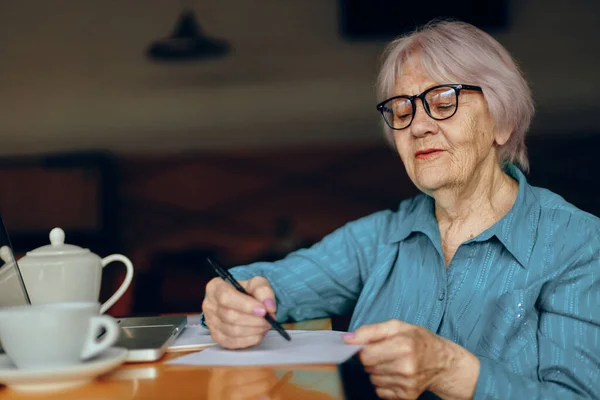 Retrato de una anciana con gafas sentada en una mesa frente a un portátil Estilo de vida inalterado — Foto de Stock