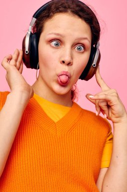 Neşeli kadın kulaklıkla müzik dinliyor turuncu süveter duyguları değişmeden izole edilmiş arka planlar