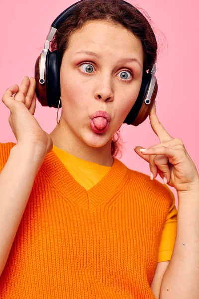 Fröhliche Frau hört Musik mit Kopfhörern orange Pullover Emotionen Spaß isolierte Hintergründe unverändert — Stockfoto