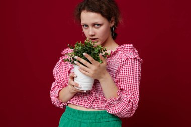 Ayakta duran ve saksıda çiçekleri tutan genç bir kadın.