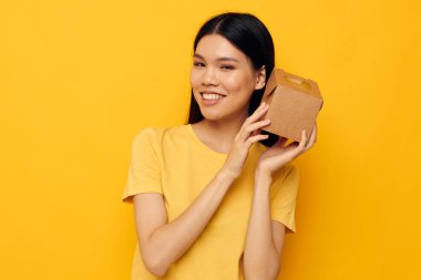 Sarı tişörtlü, elinde bir kutuyla neşeli bir kadın.