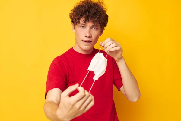 Portrait d'un jeune homme bouclé dans un t-shirt rouge protection masque médical fond jaune inaltéré — Photo