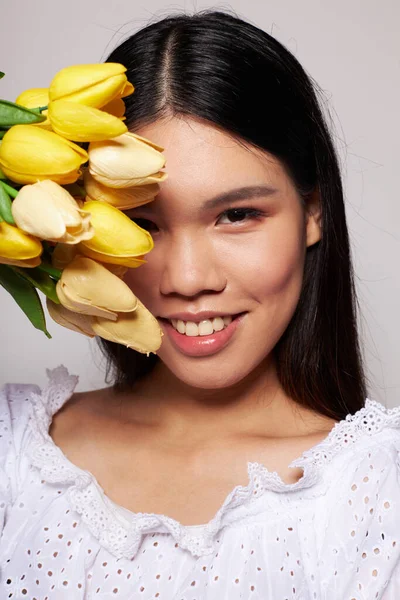 Asyalı görünümlü bir kadın çiçekler arkaplanda hafif bir poz veriyor. — Stok fotoğraf
