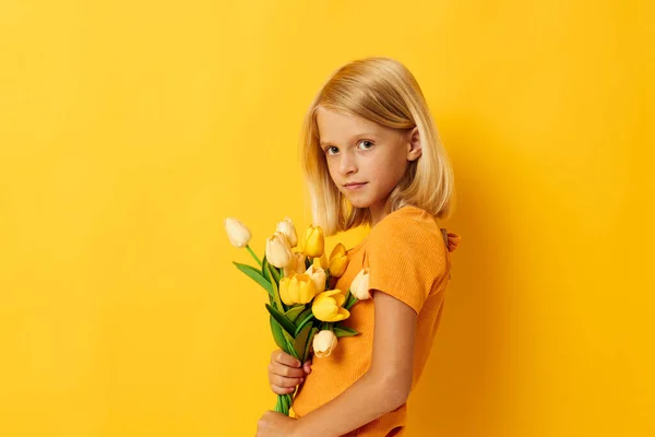 Little girl with blond hair with a bouquet of yellow flowers on a yellow background — Stockfoto