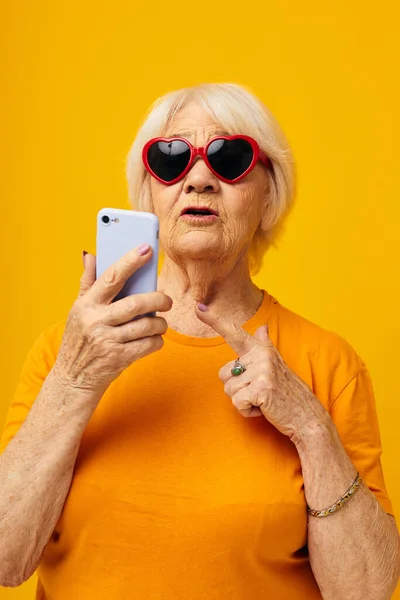 Smiling elderly woman in casual t-shirt communication by phone yellow background — Stock Fotó