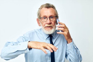 Yaşlı gri saçlı, gömlekli, kravatlı adam telefonda konuşuyor.