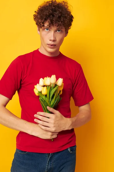 Kırmızı kıvırcık saçlı, romantik, sarı bir buket çiçekle poz veren, değişmemiş bir arka planı olan adam. — Stok fotoğraf