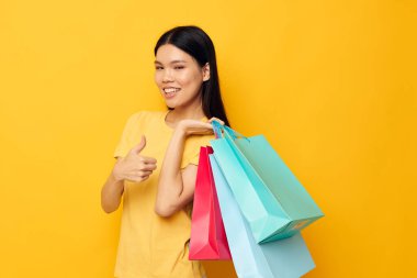 Sarı tişörtlü, çok renkli alışveriş çantalı, Asyalı güzel kadın portresi. Stüdyo modeli değiştirilmemiş.