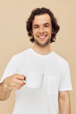 Elinde beyaz bir kupayla çekici bir adam. Duyguları bej arka planda.