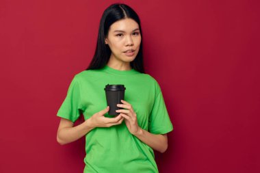 Yeşil tişörtlü çekici genç Asyalı kadın. Bir bardak içki. Eğlenceli stüdyo modeli.