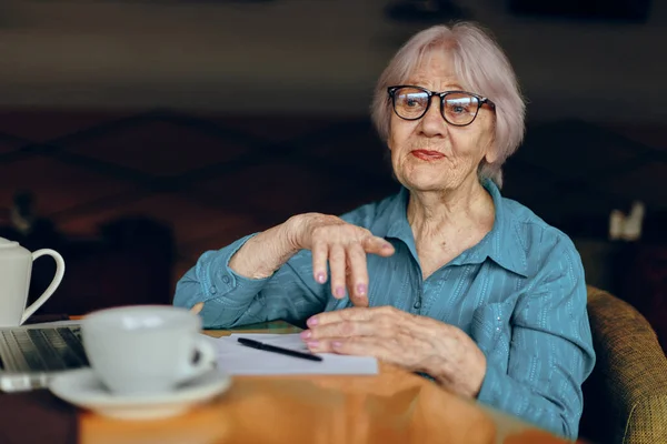 Mujer mayor sentada en un café con una taza de café y una computadora portátil Redes sociales inalteradas — Foto de Stock