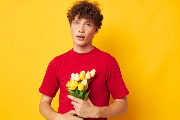 Retrato de un joven rizado en una camiseta roja un ramo de flores regalo de vacaciones monocromo tiro — Foto de Stock