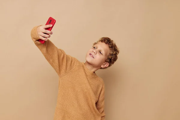 Cheerful boy with red phone in hands posing beige background
