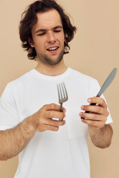 Hombre atractivo en una camiseta blanca con cuchillo con tenedor fondo aislado —  Fotos de Stock