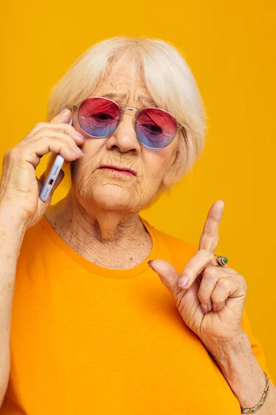 Emekli yaşlı bir kadının mutlu bir hayat tarzı fotoğrafı. Sarı tişörtlerle, telefonlara yakın duygularla. — Stok fotoğraf