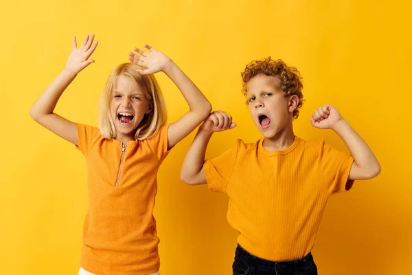 Menino e menina em camisetas amarelas de pé lado a lado emoções da infância fundo amarelo — Fotografia de Stock
