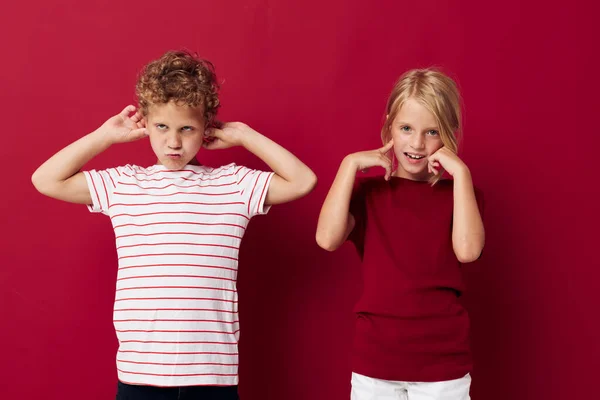 Lindos niños preescolares sonriendo y posando en ropa casual sobre fondo rojo — Foto de Stock