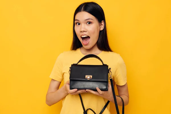 Porträtt asiatisk vacker ung kvinna med en svart kvinna väska i händerna gul bakgrund oförändrad — Stockfoto