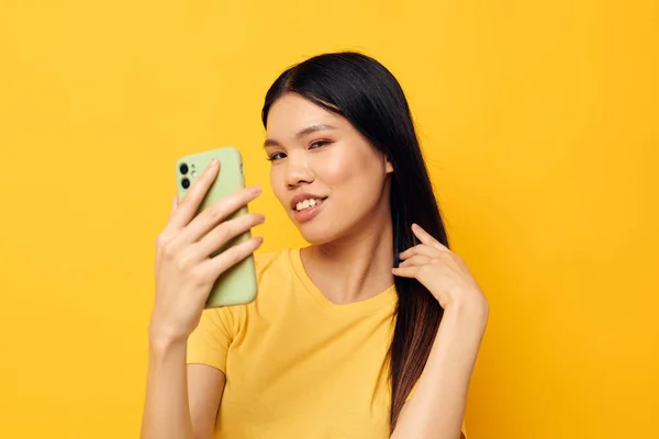 Γυναίκα με ασιατική εμφάνιση σε ένα κίτρινο t-shirt κοιτάζοντας το τηλέφωνο θέτοντας μοντέλο στούντιο αναλλοίωτη — Φωτογραφία Αρχείου