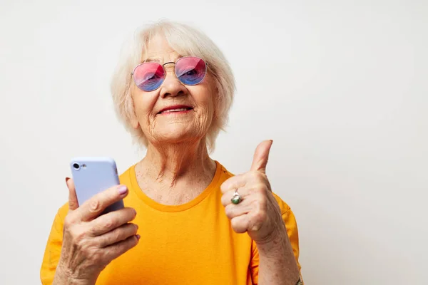 Foto de anciana jubilada en gafas de moda con un teléfono inteligente en la mano emociones de primer plano — Foto de Stock