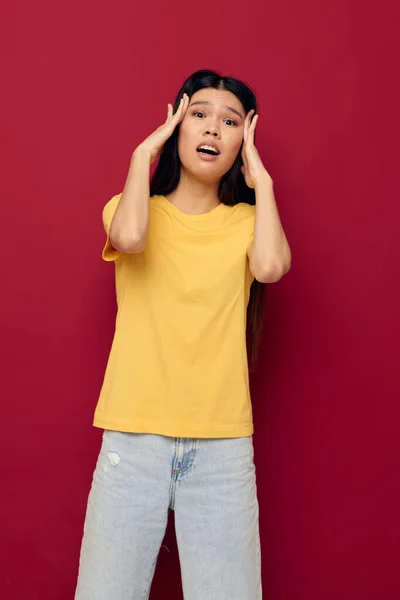 Mulher com aparência asiática gestos com as mãos em um amarelo t-shirt casual desgaste vermelho fundo inalterado — Fotografia de Stock