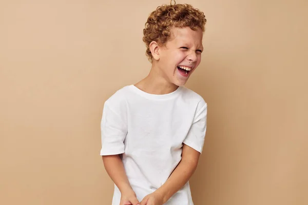 Ricci ragazzo in un bianco t-shirt posa divertente beige sfondo — Foto Stock
