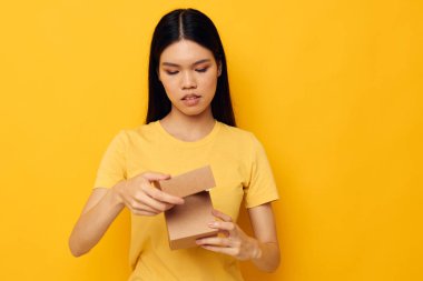 Elinde küçük bir kutu hediye taşıyan kadın. Sarı arka plan.