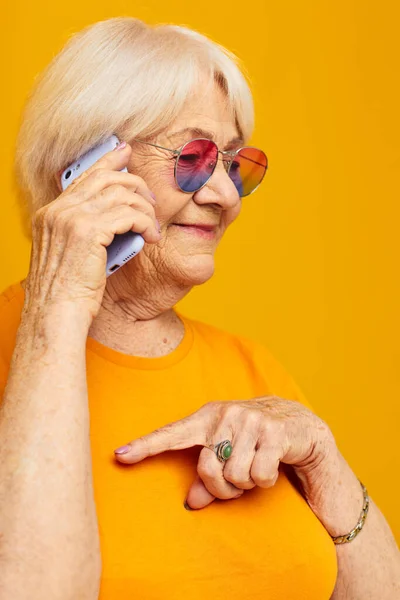 노란 배경 전화로 가볍게 티셔츠를 입고 대화를 나누는 나이든 친절 한 여성의 모습 — 스톡 사진