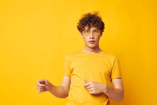 Genç kıvırcık saçlı adam sarı t-shirt gözlükleri moda el hareketleri tek renkli fotoğraf — Stok fotoğraf