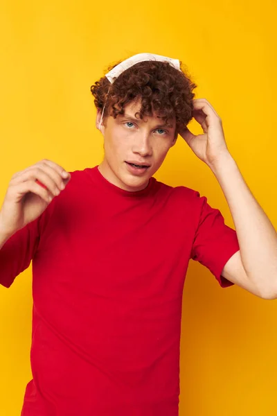 Tipo con el pelo rizado rojo en una camiseta roja máscara médica protección fondo amarillo inalterado —  Fotos de Stock