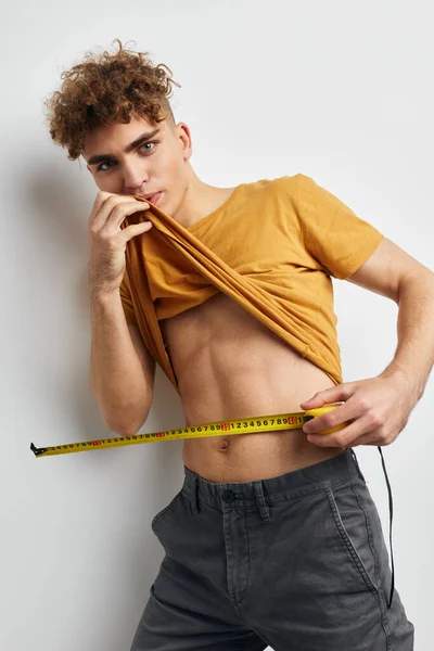 Guapo joven medida cinta métrica en amarillo camiseta fondo claro —  Fotos de Stock