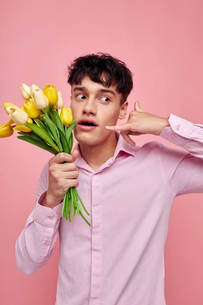 Красивий хлопець в рожевій сорочці з букетом квітів жестикулює руками ізольований фон незмінний — стокове фото