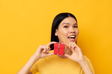 Çekici genç Asyalı kadın elinde bir hediye kutusu tutuyor. Arka planda bir değişiklik olmamış gibi duruyor.