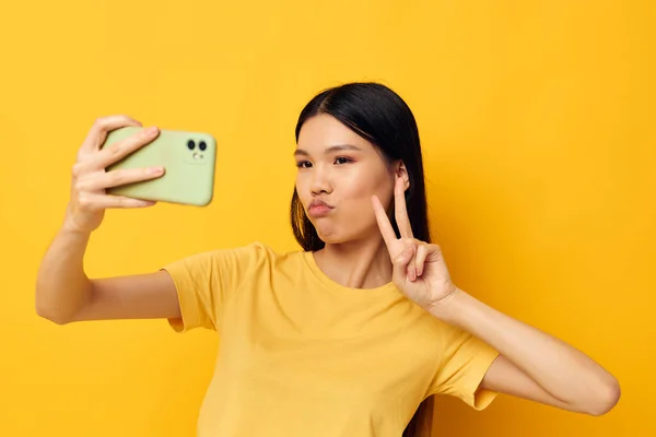 노란 티셔츠를 입은 여성 이 아무런 변화 없이 노란 배경 사진을 찍고 있는 전화를 보고 있습니다. — 스톡 사진