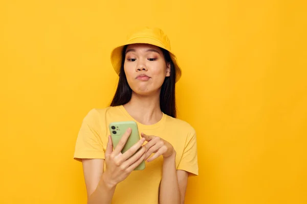 노란 모자와 티셔츠를 입은 젊은 아시아 여성 이 전화 스튜디오 모델로 변경되지 않은 대화를 하는 모습 — 스톡 사진