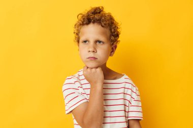 Kıvırcık saçlı, çizgili tişörtlü sarı arka planlı çocuk.