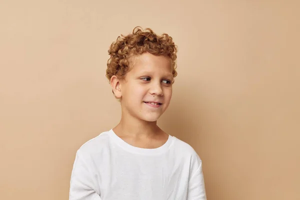 Veselý chlapec s kudrnatými vlasy v bílém tričku béžové pozadí — Stock fotografie