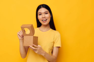 Sarı tişörtlü, elinde bir kutuyla neşeli bir kadın.