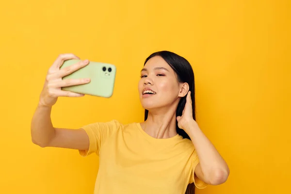 Mulher com aparência asiática em uma camiseta amarela olhando para o telefone posando Monocromático tiro — Fotografia de Stock
