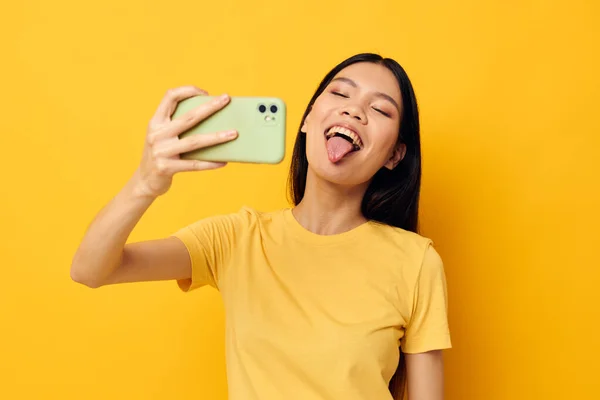 Encantadora joven asiática con una camiseta amarilla mirando el teléfono posando estilo de vida inalterado — Foto de Stock