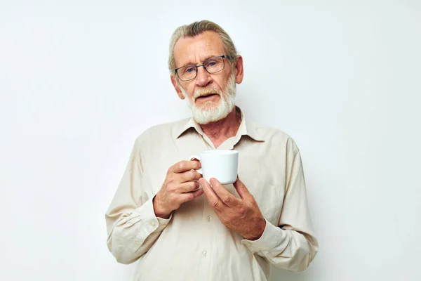 Old man in glasses with a mug on a white background and a white shirt — Stock fotografie