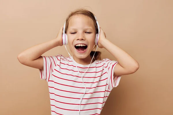 Bambina a righe t-shirt cuffie gesto mani sfondo beige — Foto Stock