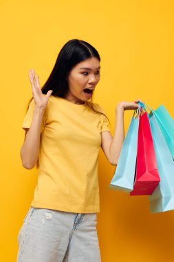 Sarı tişörtlü, çok renkli alışveriş çantalı, Asyalı güzel kadın portresi. Stüdyo modeli değiştirilmemiş.